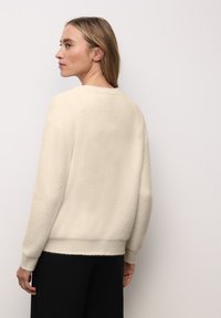 Sweter w kolorze kremowym o miękkiej fakturze, z okrągłym dekoltem i luźnym krojem. Posiada lekko skrócone rękawy oraz prążkowany dół.