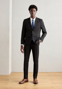 Schwarzer Anzug mit schlanker Passform, weißem Hemd und blauer Krawatte. Braune Leder Schuhe. Glatte Textur, modernes Design, minimalistischer Stil.