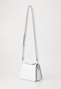 White faux leather handbag with a gold zipper, adjustable gray strap, and black piping. Features a structured, trapezoidal shape.