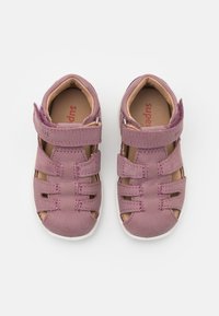 Pink leather sandals with cut-out design, adjustable strap, and white rubber sole. Features stitched detailing and a textured finish.