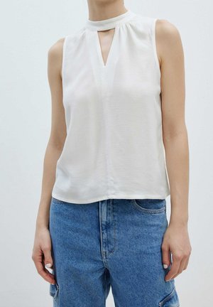 Ærmeløs hvid bluse med høj hals og nøglehul-detalje foran. Glat tekstur, løs pasform, parret med højtaljede blå denim jeans.