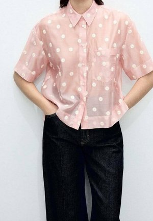 Light pink short-sleeve shirt with white daisy patterns, button-up front, and a single chest pocket, paired with dark blue denim pants.