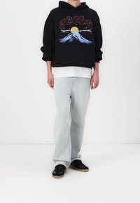 Svart hoodie med berggrafik, lager på en vit T-shirt. Ljusblå vida jeans och svarta sneakers med gummisålar.