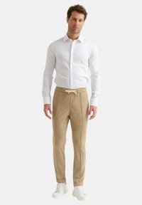 Camicia bianca con bottoni abbinata a pantaloni jogger beige con coulisse e piping laterale, completati da sneaker bianche.