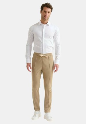 Camicia bianca con bottoni abbinata a pantaloni jogger beige con coulisse e piping laterale, completati da sneaker bianche.