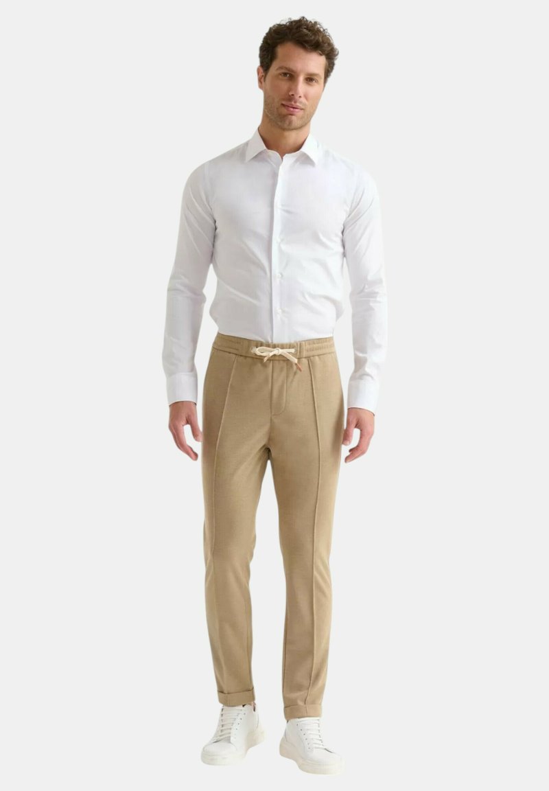 Camicia bianca con bottoni abbinata a pantaloni jogger beige con coulisse e piping laterale, completati da sneaker bianche.