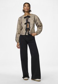 Jaqueta cropped com padrão de leopardo, laços pretos, punhos elásticos, combinada com calças largas pretas de cintura alta e sapatos casuais.