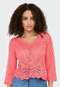 Pull en tricot corail avec un col en V, des manches trois-quarts et un ourlet festonné. Le design ajouré met en avant un motif en zigzag.