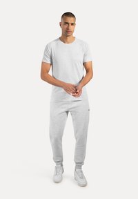 Lys grå bomulds T-shirt og matchende sweatpants med en glat tekstur. Outfittet har et lille logo på brystet. Hvide sneakers fuldender looket.