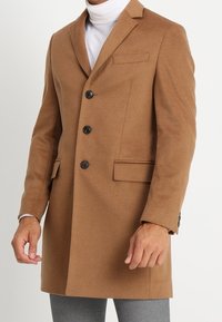 Brauner Wollmischmantel mit strukturierten Schultern, Reverskragen, vier Knöpfen, zwei frontalen Taschen und einer glatten Textur.
