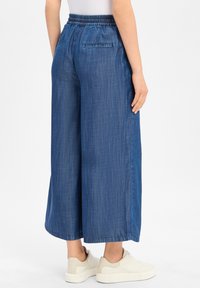 Weite Jeanshose mit elastischem Bund in einem mittleren Blauton. Verfügt über zwei Gesäßtaschen und eine glatte, weiche Textur.