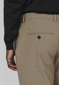 Pantalons kaki avec une finition texturée, dotés d'une poche arrière fermée par un bouton noir et d'un léger pli repassé le long de la jambe.