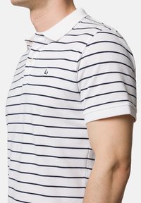 Biała koszulka polo w granatowe poziome paski, klasyczny kołnierzyk, trzy guziki i małe logo na klatce piersiowej. Krótkie rękawy i teksturowany materiał.