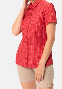 Camicia a maniche corte a scacchi rossi con colletto, chiusura a bottoni e un accento con logo. Abbinata a pantaloni corti beige chiaro, che mostrano un design casual.
