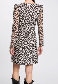 Robe longue à manches longues en beige avec un motif abstrait noir, cintrée à la taille, dévoilant une légère silhouette évasée à l'ourlet.