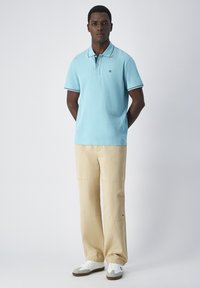 Jasnoniebieska koszulka polo z kołnierzykiem i kontrastowymi granatowymi wykończeniami, zestawiona z beżowymi spodniami typu wide-leg i białymi trampkami. Prosty design i wygodne dopasowanie.