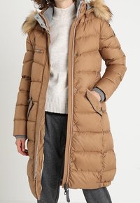 Abrigo acolchado marrón con cierre frontal, capucha desmontable con forro de piel, bolsillos laterales y puños acanalados. Presenta un diseño acolchado y un aislamiento cálido.