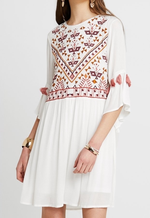 Vestido blanco con un cuerpo bordado de patrones en tonos burdeos y naranja, con mangas acampanadas con flecos y una falda fluida.
