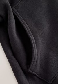 Gros plan d'une poche en tissu noir avec des coutures visibles sur un vêtement à texture douce.