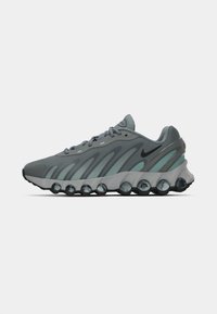 Sport sneakers with a gray mesh upper, green accents, and a chunky black sole featuring visible cushioning pods. Laces are threaded through reinforced eyelets.