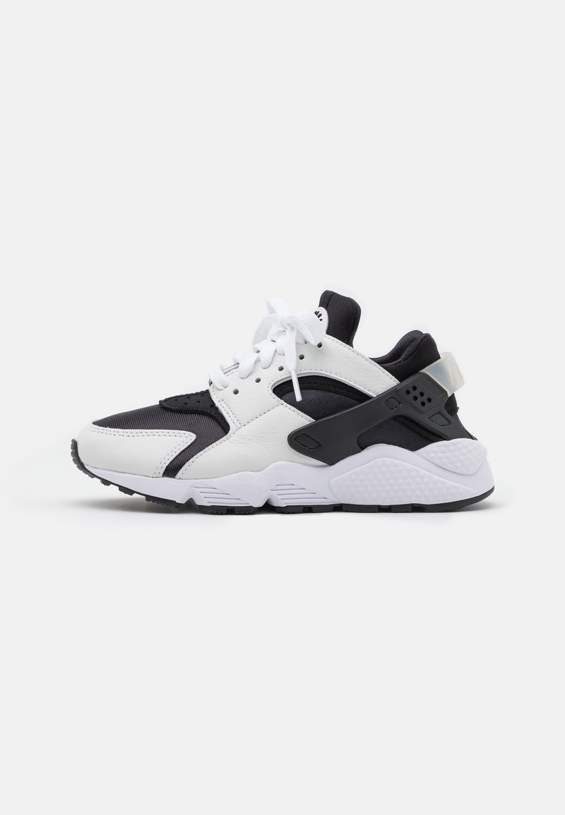 Baskets athlétiques noir et blanc avec lacets blancs, semelle coussinée et soutien de talon en plastique noir sur un fond uni.
