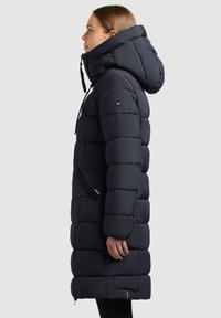 Geacă puffer bleumarin cu guler înalt și glugă ajustabilă, cu un design pătrat matlasat și două buzunare laterale.