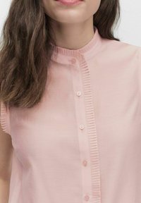 Lyserød bluse med ståkrave, frontlås med knapper og lodrette plissé-detaljer langs knaplisten. Blødt, glat stof.
