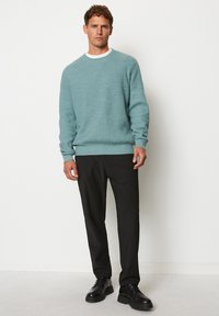 Helles türkisfarbener gerippter Pullover mit langen Ärmeln, Rundhalsausschnitt und solider Textur, kombiniert mit schwarzen Hosen und schwarzen Schnürschuhen.