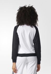 Svart och vit sportig sweatshirt med raglanärmar, med en strukturerad tyg och ribbade ärmslut, visad från baksidan.