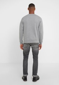 Sudadera gris de cuello redondo, combinada con jeans gris oscuro. El conjunto presenta una textura lisa con puños enrollados y un diseño ajustado.