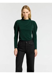 Grön, glittrig långärmad topp med hög krage och rynkade axlar, ihop med svarta raka byxor.