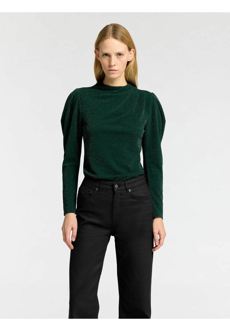 Grön, glittrig långärmad topp med hög krage och rynkade axlar, ihop med svarta raka byxor.