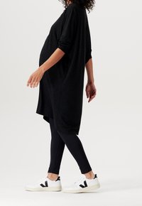 Top negro de gran tamaño con mangas largas, usado sobre leggings negros y zapatillas blancas. Presenta un corte relajado y una textura suave.
