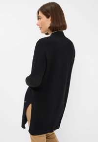 Schwarzer gestrickter Pullover mit langen Ärmeln, einem hohen Kragen und seitlichen Schlitzen. Verfügt über eine strukturierte Oberfläche und kleine silberne Knöpfe am Saum.