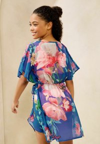 Prosojen, modri cvetlični kimono s kratkimi rokavi, ki vsebuje rože v rožnati in vijolični barvi, s pasom za zavezovanje in razporkom za lažje gibanje.
