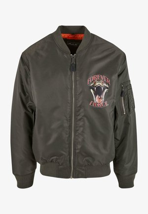 Olivovo zelená bomber bunda so stojacím golierom, zipsom, rebrovanými manžetami a grafikou "NAVŽDY ODVAŽNÁ", ktorá zobrazuje hada na hrudi.