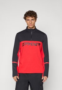Langarm pullover in rood en zwart. Voorzien van een halve rits kraag, contrasterende zijpanelen en een gedurfd zwart "SPYDER" logo over de borst.