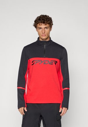 Langarm pullover in rood en zwart. Voorzien van een halve rits kraag, contrasterende zijpanelen en een gedurfd zwart "SPYDER" logo over de borst.