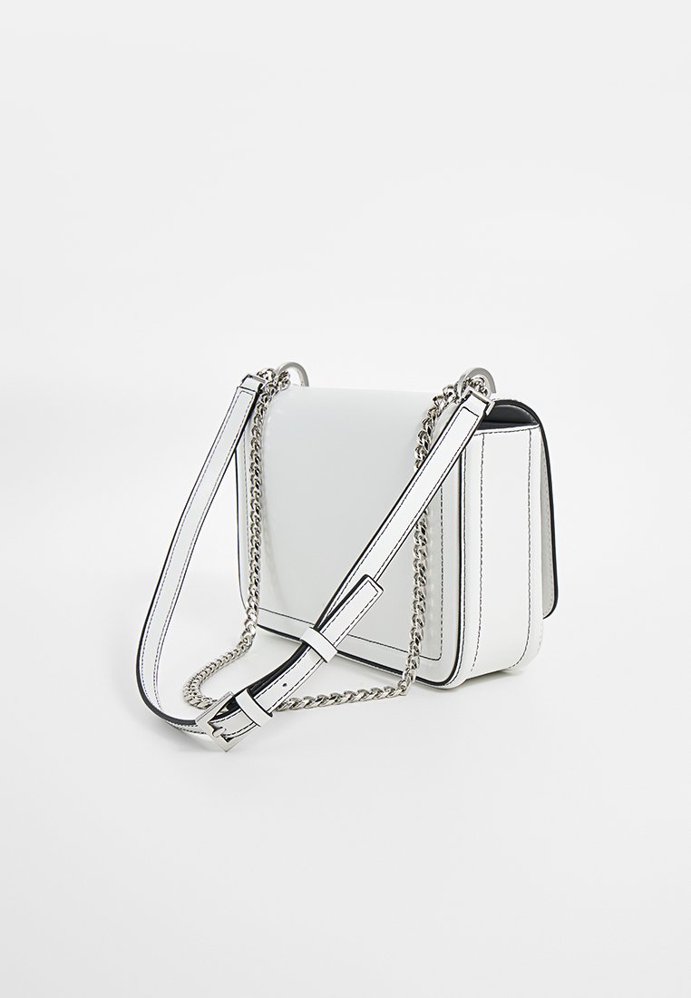 Sac à bandoulière en cuir blanc avec des coutures noires, de forme rectangulaire, chaîne et sangle réglable, présentant un design épuré et minimaliste.