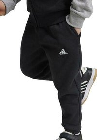 Pantaloni da jogging neri in tessuto morbido, con vita elastica, tasche laterali e logo Adidas ricamato in bianco.