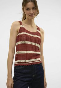 Rood en crèmekleurig gestreept gehaakt tanktop met een scalloped zoom, met brede schouderbanden en een open weefstructuur. Gecombineerd met donkere spijkerbroeken.