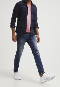 Mörkblå rutig skjorta som är knäppt över en rosa V-ringad t-shirt, i kombination med blå jeans och vita sneakers, vilket visar en avslappnad outfit.