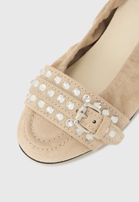 Μπεζ σουέντ μπαλαρίνες με φαρδιά λουρί που διακοσμείται με διαυγείς κρυστάλλους και ασημένια αγκράφα, με στρογγυλεμένη μύτη και απαλό υφασμάτινο υφή.