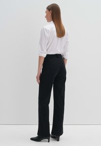 Schwarze High-Waist-Jeans mit geradem Bein und minimalistischem Design. Kombiniert mit einem weißen Hemd und schwarzen Absatzschuhen.