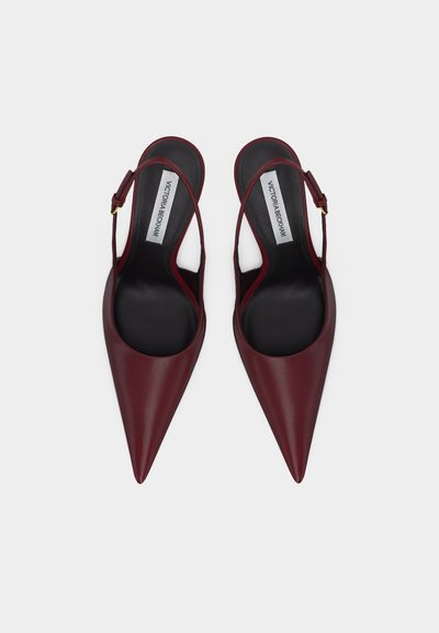 Par rdeče temnih usnjenih salonarjev z ozkim spicom, odprtim zadnjim delom in črnimi vložki ter nastavljivimi paščki okoli gležnjev, označeni z imenom Victoria Beckham.