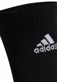 Chaussette de sport en coton noir avec texture côtelée, arborant un logo Adidas brodé en blanc sur le côté.