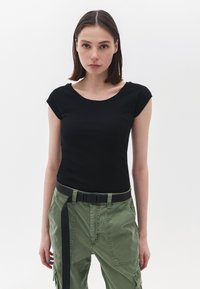Top aderente nero a maniche corte con scollatura a dolcevita abbinato a pantaloni cargo verdi oliva. I pantaloni presentano una cintura nera con fibbia e tasche.