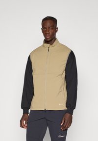 Gilet leggero beige con colletto alto, maniche nere a contrasto e chiusura a zip. Presenta un logo all'orlo e una texture liscia.