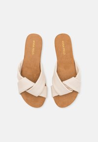 Sandales à glisser beiges avec un design à bande croisée, fabriquées à partir de matériaux souples. Semelle intérieure en liège et texture lisse. Nom de la marque embossé sur la semelle.