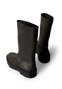 Botas de goma verdes hasta el tobillo con acabado mate, punta redondeada, suela exterior plana negra y una sutil marca en el talón.